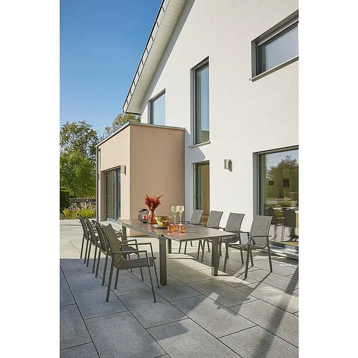 Sunfun Maja Gartenmöbel-Set Stone - 9 -tlg., Sintered Stone, Aluminium, Textilen, Anthrazit, Tischplatte ausziehbar - Ein moderner Gartentisch mit Stühlen auf einer Terrasse vor einem stilvollen Haus, ideal für Mahlzeiten im Freien.