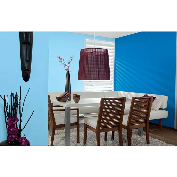 Alpina Vollton- & Abtönfarbe Color - Royal Blue, Matt, 250 ml, Lösemittelfrei - Ein Esstisch mit vier Stühlen unter einer dekorativen Lampe, ergänzt durch Vasen und eine afrikanische Maske an der blau gestrichenen Wand.