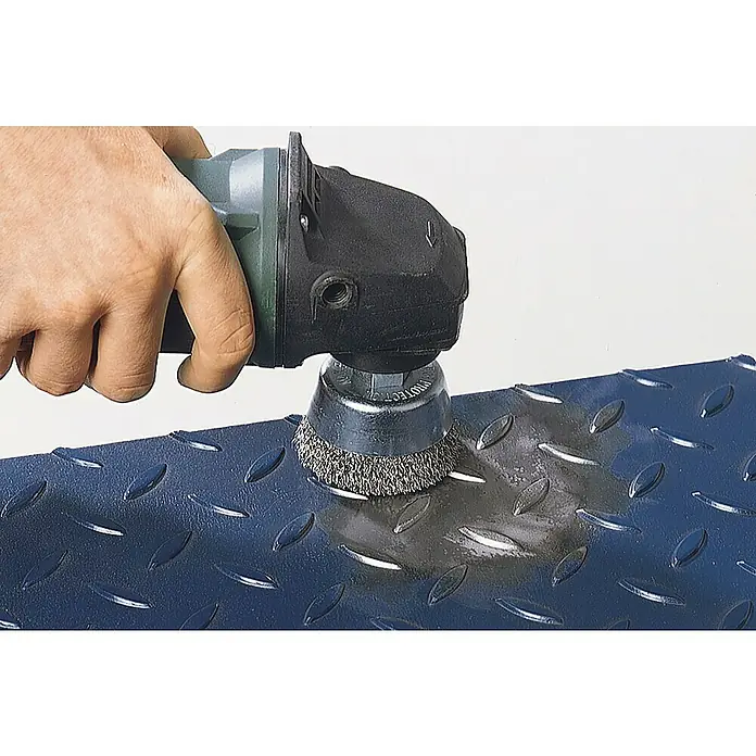 Wolfcraft Topfbürste - Edelstahl, 70 mm, Gewellt - Eine Drahtbürste, die an einem Winkelschleifer befestigt ist, wird zum Reinigen und Glätten einer strukturierten Metalloberfläche verwendet.