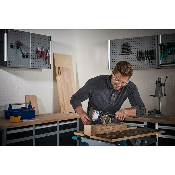 Wolfcraft Holz-Strukturbürste - Durchmesser: 80 mm - Mann benutzt eine Drahtbürste an einer Bohrmaschine, um Holz zu bearbeiten. Werkzeuge hängen an einer Lochwand im Hintergrund.