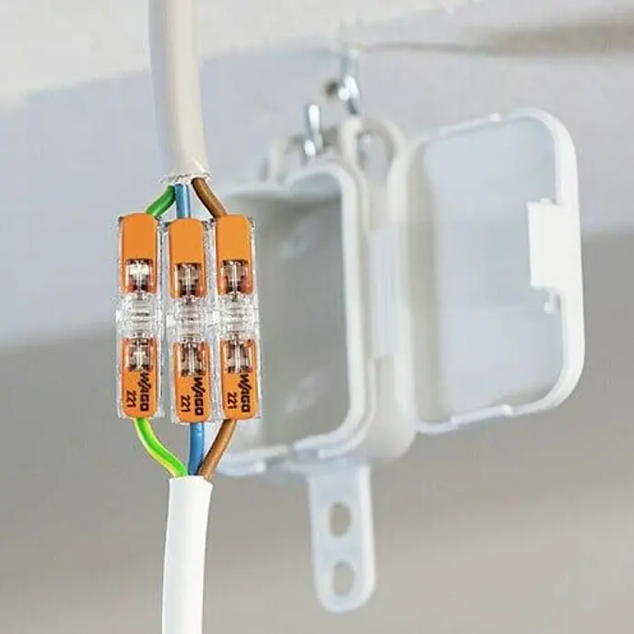 Wago Durchgangsklemme 221-2411 mit Hebeln - 12 Stk., 0,2 mm² - 4 mm² - Nahaufnahme von Wago 221-Klemmen mit weißem Kabel, das an einer Abzweigdose mit offenem Deckel befestigt ist. Praktische Verbindungstechnik für Elektroinstallationen.