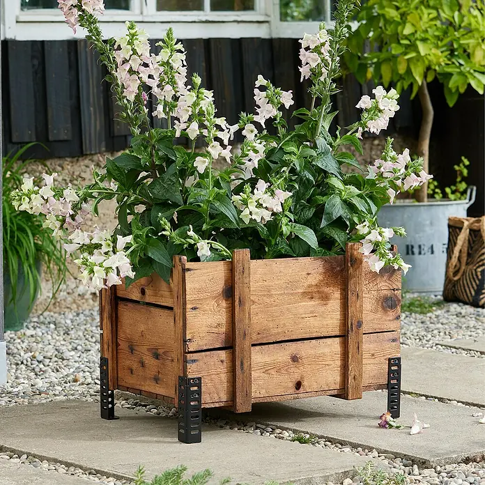 Wagner System Möbelfuß - Höhe: 12 cm, Stahl, Schwarz - Nahaufnahme eines rustikalen Holzpflanzgefäßes mit blühenden weißen und rosa Blumen, das auf einem gepflasterten Bereich steht.