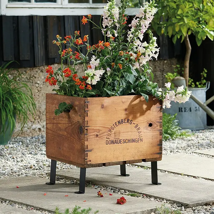 Wagner System Möbelfuß - Stahl, L x H: 5 x 12 cm - Blumenkasten aus Holz mit dem Aufdruck Fürstenberg-Brau Donaueschingen und mit Blumen bepflanzt.