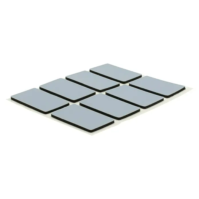 Wagner System Möbelgleiter - 16 x 26 mm, Kleben, 16 Stk. - Nahaufnahme von acht grauen, rechteckigen Wärmeleitpads auf einer weißen Schutzfolie, die für die Wärmeableitung in elektronischen Geräten verwendet werden.