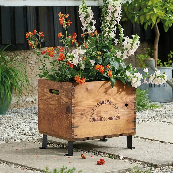Wagner System Möbelfuß - Stahl, L x H: 5 x 8 cm - Blumenkasten aus Holz mit Aufschrift und Metallbeinen, bepflanzt mit orangefarbenen und weißen Blumen.