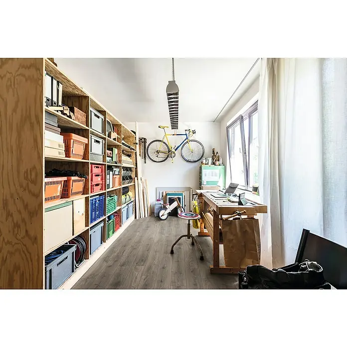 Krono Original Laminat Atlantic 12 - Steelworks Oak, Landhausdiele, 1.288 x 195 x 12 mm - Übersichtliches Bild eines Hobbyraums mit Holzregalen, einem Fahrrad an der Wand und einem Werkzeugtisch am Fenster für kreatives Arbeiten.