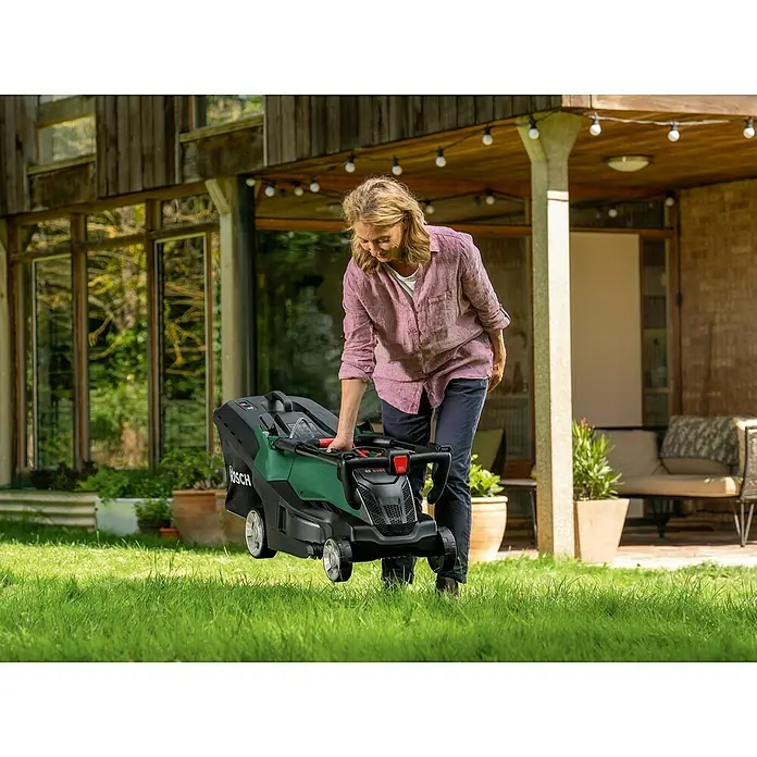 Bosch Elektro-Rasenmäher AdvancedRotak 44-750 - 1.800 W, Schnittbreite: 44 cm - Frau hebt einen Bosch Akku-Rasenmäher auf dem Rasen an. Der Rasenmäher ist grün und schwarz.