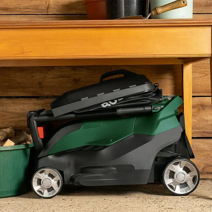 Bosch Elektro-Rasenmäher AdvancedRotak 44-750 - 1.800 W, Schnittbreite: 44 cm - Ein grüner Bosch Rasenmäher mit Fangkorb steht platzsparend unter einem Tisch, ideal für kleine Gärten und einfache Lagerung.