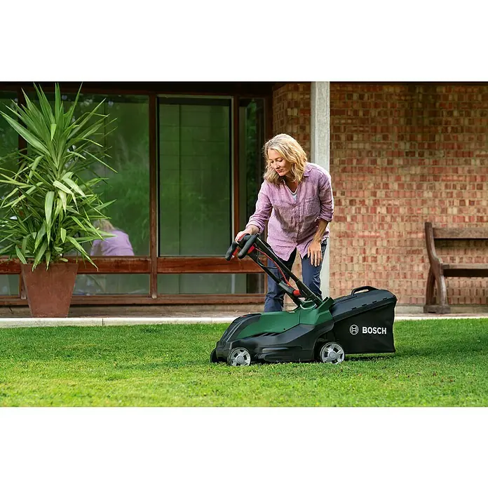 Bosch Elektro-Rasenmäher AdvancedRotak 44-750 - 1.800 W, Schnittbreite: 44 cm - Frau benutzt einen Bosch Rasenmäher auf einem grünen Rasen vor einem Haus. Der Rasenmäher ist grün und schwarz.