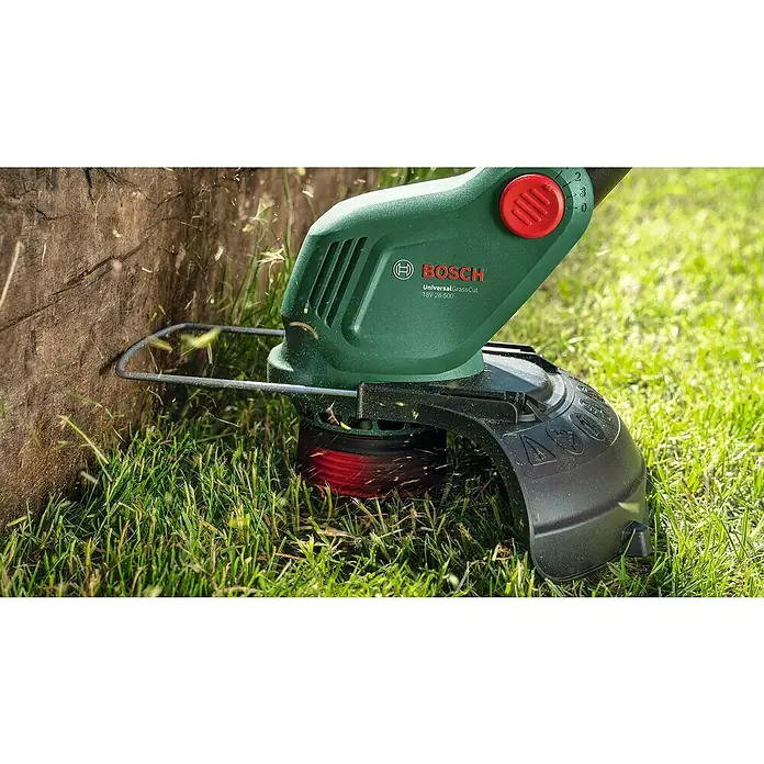 Bosch Power for All 18V Akku-Rasentrimmer UniversalGrassCut 18V-26-50018 V, Li-Ionen, Ohne Akku - Detailaufnahme eines Bosch UniversalGrassCut 18V-26-500 Akku-Rasentrimmers beim Kantenschneiden auf Rasenfläche.