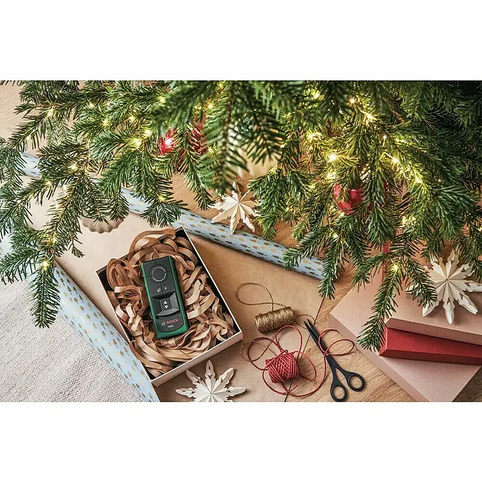 Bosch Detector Truvo II - Apto para: Detectar cables eléctricos y metal, Profundidad de detección: Máx. 70 mm de metales ferrosos - Escena de envoltorio de regalos con un telémetro Bosch verde en una caja, rodeado de adornos navideños.