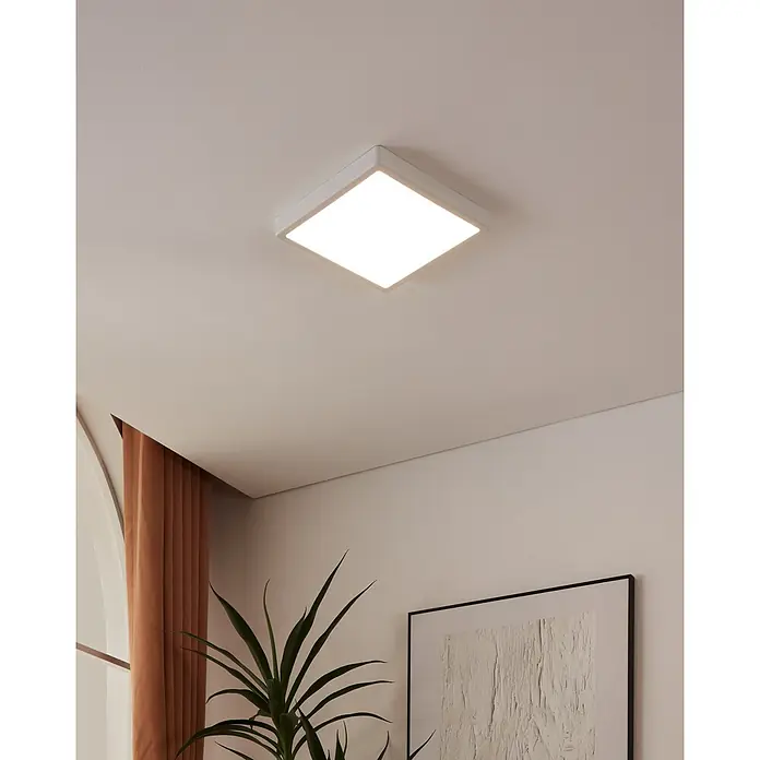 Eglo connect.z LED-Deckenleuchte FUEVA-Z - 19,5 W, L x B x H: 28,5 x 28,5 x 2,8 cm, Weiß, Eckig - Weiße, quadratische Deckenleuchte an einer hellen Decke mit einer Zimmerpflanze, Vorhängen und einem gerahmten Bild im Hintergrund.