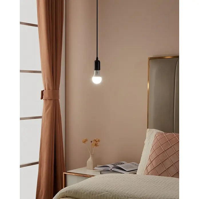 Eglo connect.z Smart-LED-Lampe Zigbee RGB/CCT - E14, Dimmbarkeit: Nicht Dimmbar, RGBW, 470 lm, 4,9 W - Nahaufnahme einer hängenden Glühbirne in einem Schlafzimmer mit Vorhängen und Nachttisch mit Lampe.