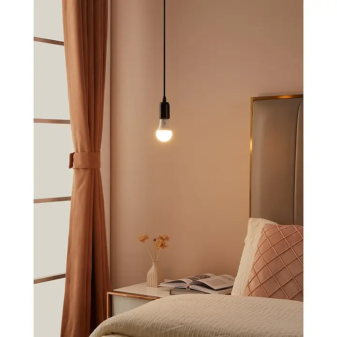 Eglo connect.z Smart-LED-Lampe Zigbee RGB/CCT - E14, Dimmbarkeit: Nicht Dimmbar, RGBW, 470 lm, 4,9 W - Das Foto zeigt eine moderne Glühbirne mit einem schwarzen Kabel, die über einem Nachttisch in einem Schlafzimmer hängt.