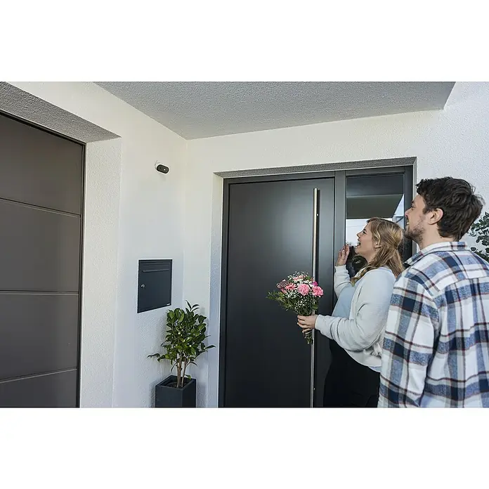 Abus Akku-Überwachungskamera PPIC91520 W PRO - Weiß - Ein Paar steht vor einer modernen Haustür mit einem schlichten Design. Eine Überwachungskamera ist über der Tür installiert.