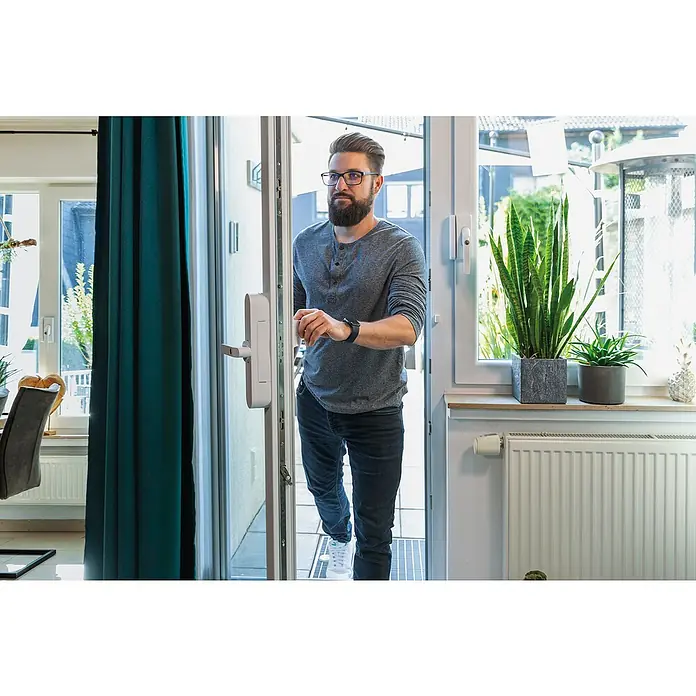 Abus Funk-Türschlossantrieb Wintecto one FCA4100 W - Geeignet für: Fenster, Weiß, Bedienung: Über App - Ein Mann öffnet eine Tür mit einem intelligenten Türschloss. Das smarte Schloss ist an der Tür befestigt und ermöglicht einen schlüssellosen Zugang.