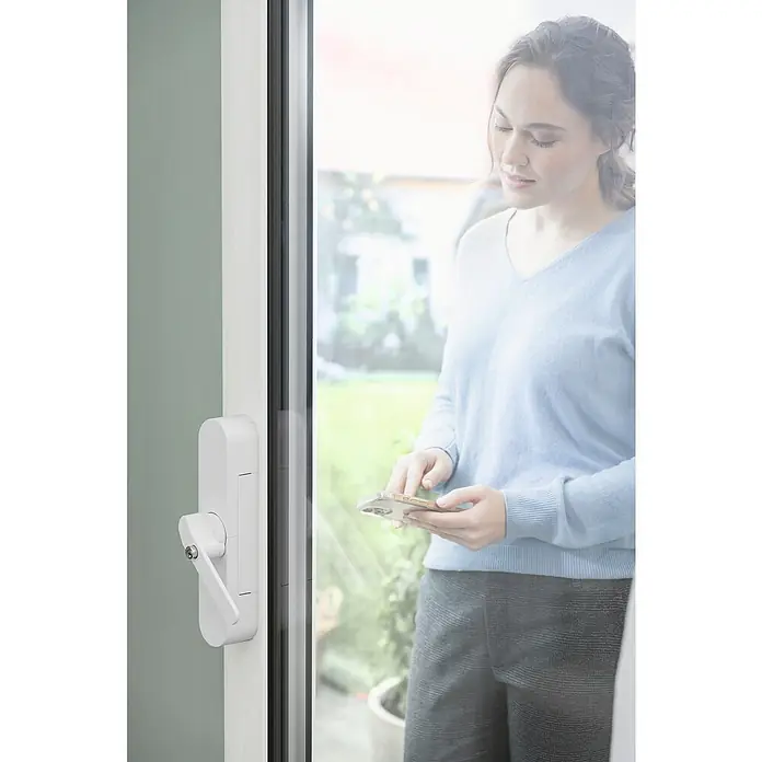 Abus Funk-Türschlossantrieb Wintecto one FCA4100 W - Geeignet für: Fenster, Weiß, Bedienung: Über App - Frau bedient Türschloss mit App am Smartphone. Das smarte Türschloss bietet Sicherheit und Komfort für Ihr Zuhause.