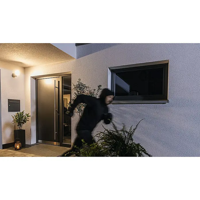 Abus Überwachungskamera PPIC46520 BK - IP66 - Einbrecher rennt an einem modernen Haus mit Fenster und Tür vorbei, möglicherweise auf der Flucht.