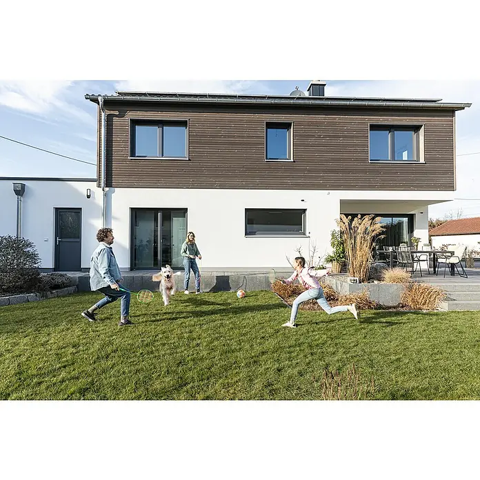 Abus Überwachungskamera PPIC46520 BK - IP66 - Eine Familie spielt Badminton im Garten ihres modernen Hauses mit großen Fenstern, die viel Tageslicht hereinlassen.