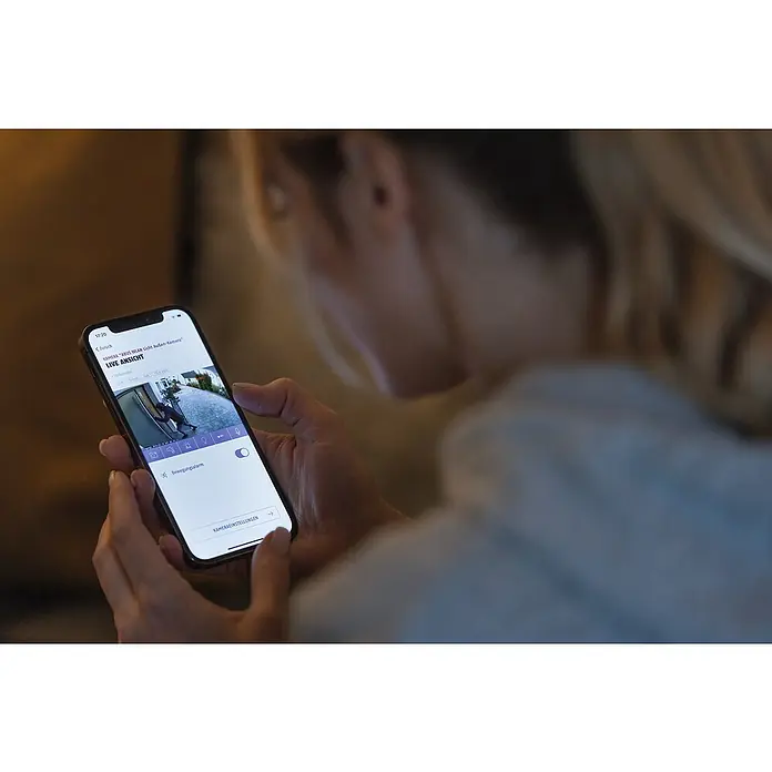 Abus Überwachungskamera PPIC46520 BK - IP66 - Frau betrachtet Smartphone mit Sicherheitskamera-App, die einen Einbrecher vor der Haustür zeigt.