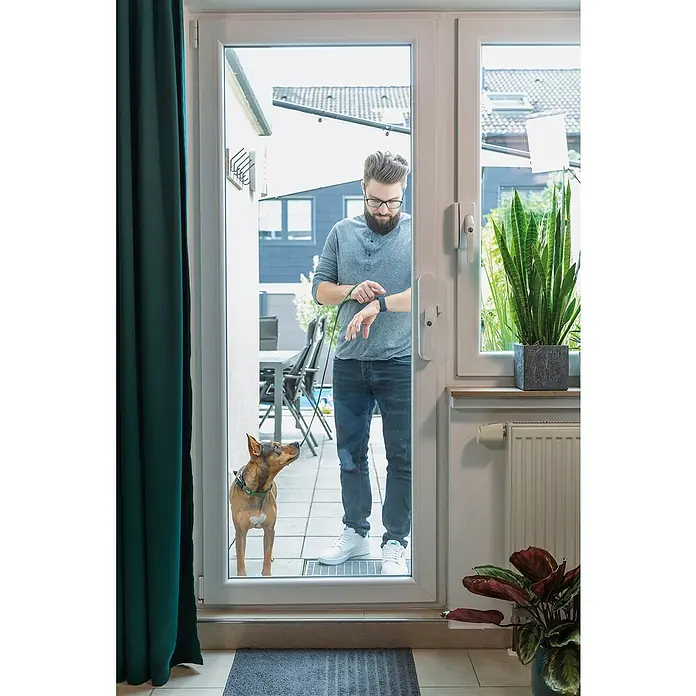 Abus Funk-Türschlossantrieb Wintecto one FCA4100 W - Geeignet für: Fenster, Weiß, Bedienung: Über App - Ein Mann mit Hund steht an einer Tür, bereit für einen Spaziergang. Der Fokus liegt auf der modernen Tür mit großzügiger Glasfläche.