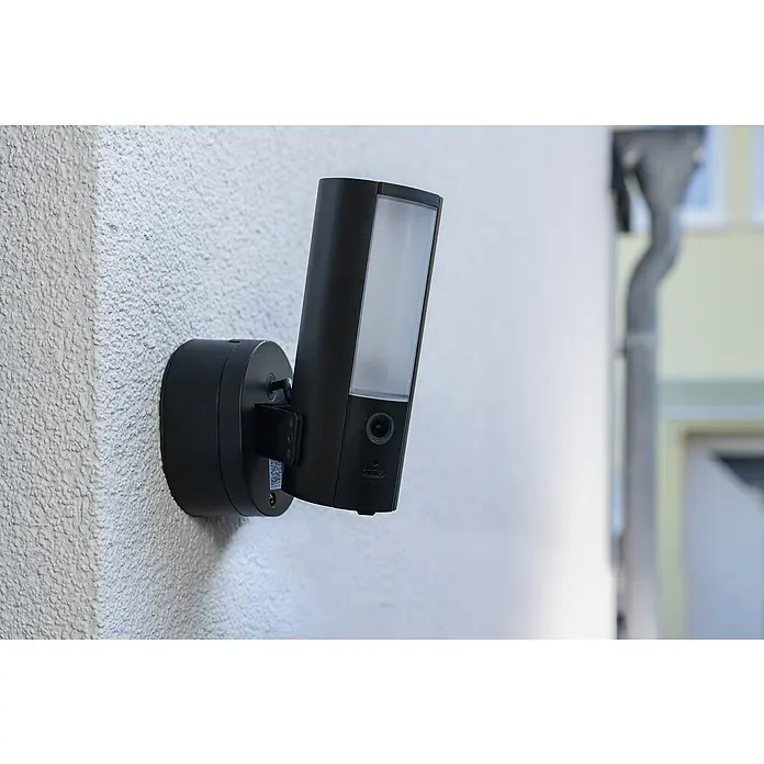 Abus Überwachungskamera PPIC46520 BK - IP66 - Nahaufnahme einer drahtlosen Aussenüberwachungskamera mit LED-Licht, die an einer strukturierten Aussenwand montiert ist.