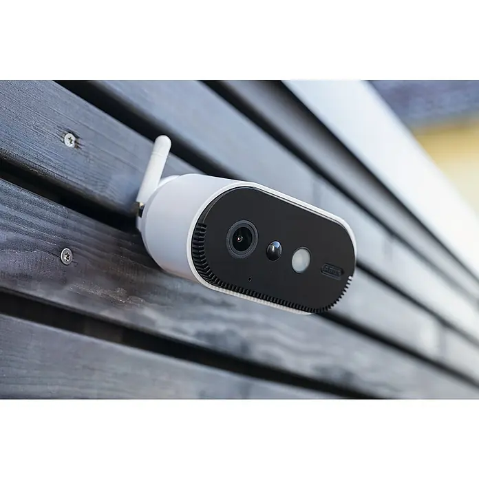 Abus Akku-Überwachungskamera-Set PPIC91000 W PRO - Weiß - Nahaufnahme einer ABUS Überwachungskamera mit Antenne, die an einer dunklen Holzfassade befestigt ist. Sie sorgt für Sicherheit im Außenbereich.