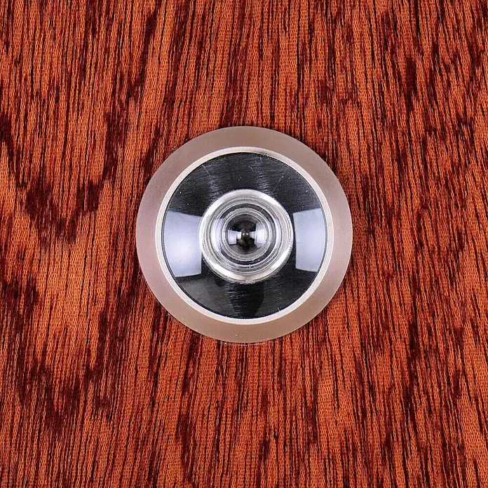 SegureStil Puerta de entrada interior S105 Serie V - 90 x 206 cm, Derecha, Sapelly, Acorazada - Primer plano de una mirilla con marco metálico en una puerta de madera, que mejora la seguridad y la privacidad.