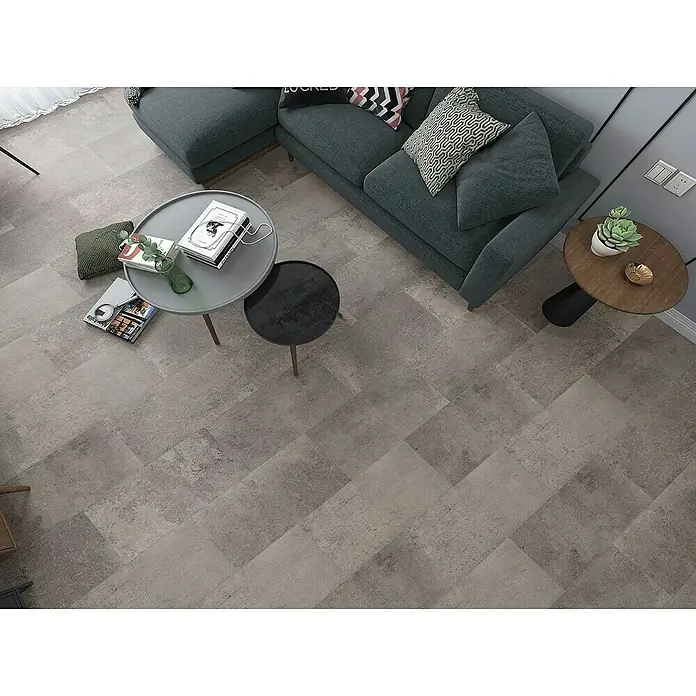 Classen Laminat Visiogrande - Concrete grey-brown, 604 x 280 x 8 mm - Eine stilvolle graue Fliesenboden-Szene mit einem Sofa, Tischen und dekorativen Elementen, die eine moderne Wohnatmosphäre schafft.