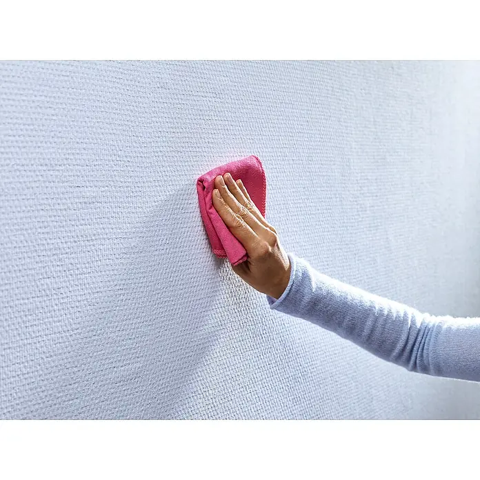 Tesa Verstellbarer Klebenagel - Geeignet für: Tapeten, Belastbarkeit: 1 kg, Weiß, 4 Stk. - Hand mit rosafarbenem Tuch reinigt eine weiße, strukturierte Wand, um Sauberkeit und Pflege im Haushalt zu demonstrieren.