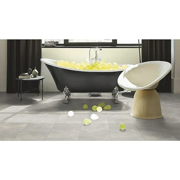 Parador Designbodenmuster Modular ONE Beton Hellgrau - 200 x 202 x 8 mm, Fliesenoptik - Ein luxuriöses Badezimmer mit freistehender Badewanne, einem Design-Sessel und stilvollen Accessoires, die eine entspannende Atmosphäre schaffen.