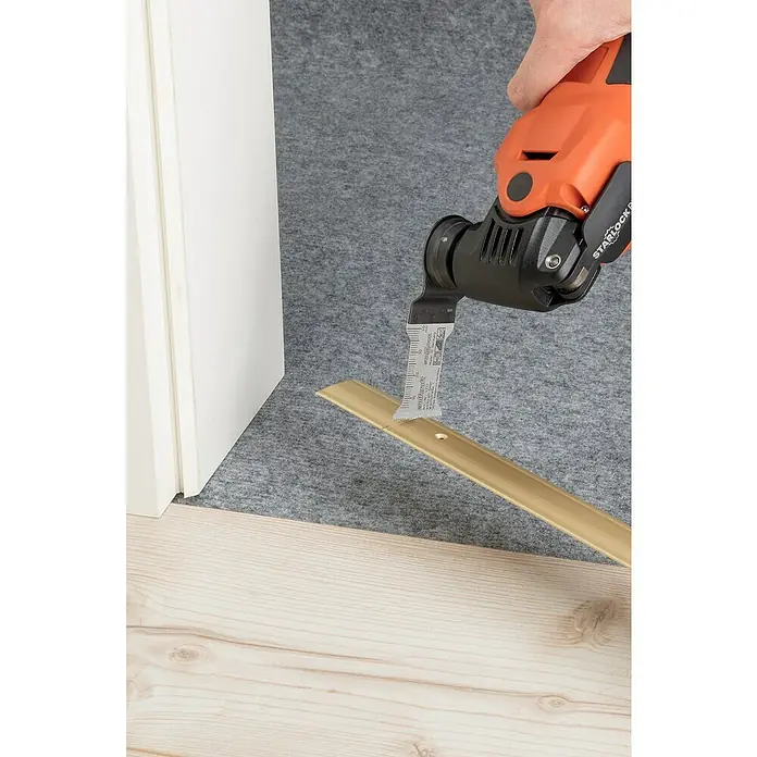 Wolfcraft Tauchsägeblatt - Geeignet für: Holz, Schnitttiefe: 40 mm - Nahaufnahme eines oszillierenden Multitools, das einen goldenen Türübergang auf einem Holzboden schneidet, ideal für Bau- und Renovierungsprojekte.