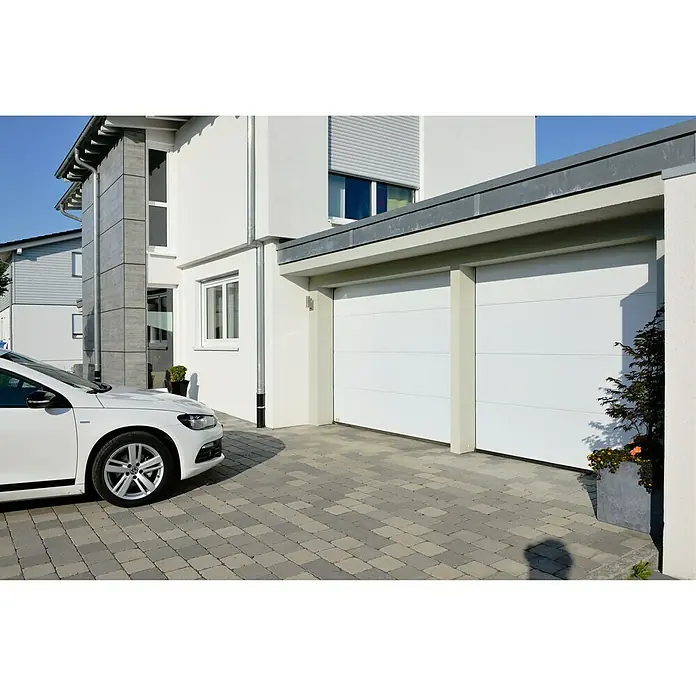 Solid Elements Garagentor Solid Pro Iso - 2.500 x 2.125 mm, Weiß - Eine moderne Doppelgarage mit weißen Toren vor einem stilvollen Haus mit gepflasterter Auffahrt und einem weißen Auto.