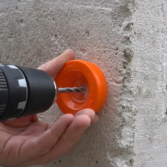 Wolfcraft Bohrstaubfänger - Durchmesser Bohrer: 4 mm - 8 mm, Kunststoff - Ein Bohrer mit einem orangefarbenen Bohreraufsatz bohrt in eine Betonwand, um ein sauberes Loch zu schaffen.