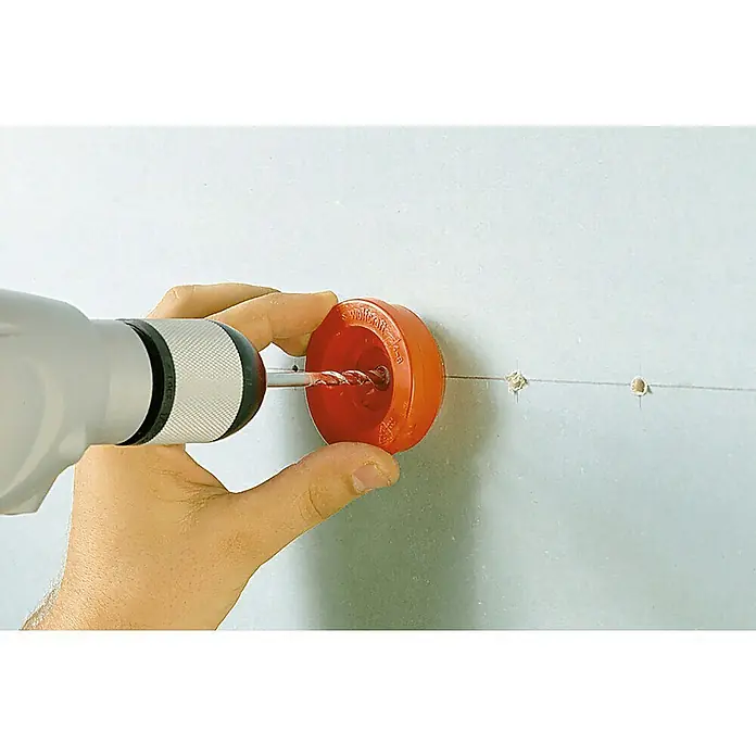 Wolfcraft Colector de polvo para taladro 2900000 - Específico para: Taladros, Plástico - Un hombre usa un taladro y una broca para hacer un agujero en una pared, utilizando un accesorio guía de taladro rojo para evitar el polvo.