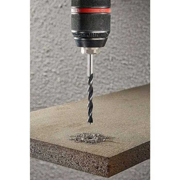 Wolfcraft Bohrer-Set - CV-Stahl, 6 -tlg. - Ein Bohrer bohrt ein Loch in ein Stück Holz, wobei Späne entstehen. Der Bohrer ist in einer Bohrmaschine befestigt.