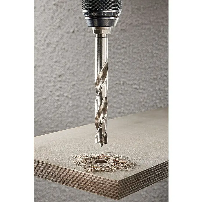 Wolfcraft Holzbohrer HSS Professional - Durchmesser Bohrer: 10 mm - Nahaufnahme eines Spiralbohrers, der ein Loch in ein Holzbrett bohrt, umgeben von Holzspänen vor einem grauen Hintergrund.
