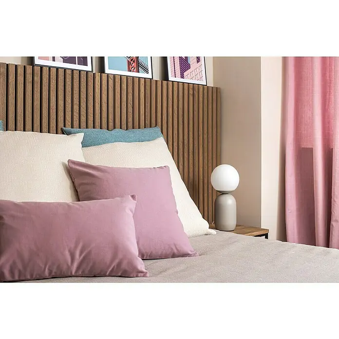 Cojín Kiron - 60 x 60 cm, Textil, Crudo - Primer plano de una cama con cabecero de madera, almohadas claras y cojines decorativos rosas, complementado con una lámpara moderna.