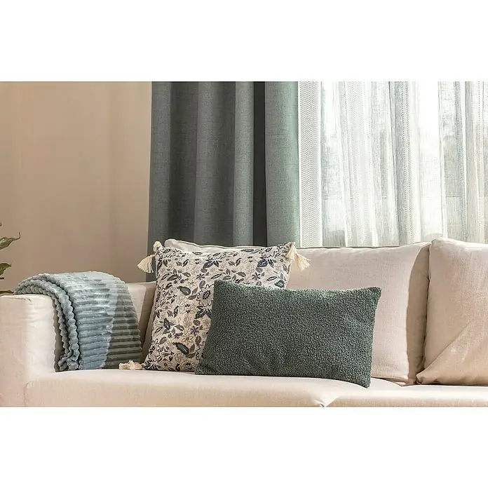 Manta para sofá Alpes - 180 x 200 cm, Poliéster, Verde - Primer plano de un sofá beige adornado con cojines decorativos y una manta azul claro, con un fondo de cortina.