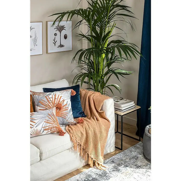Manta para sofá Eira - 130 x 170 cm, Poliéster, Melocotón - Escena de salón con sofá blanco, cojines, una manta y una planta de interior que crean un ambiente acogedor.