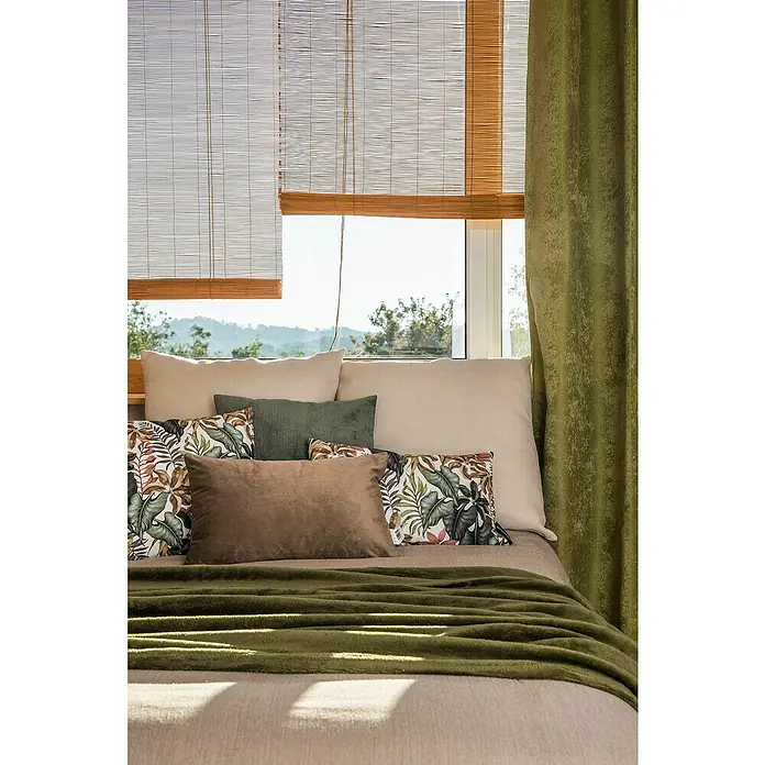 Cojín Velvet - 30 x 50 cm, Textil, Topo, Rectangular - Primer plano de una cama con muchas almohadas y una manta verde, situada frente a una ventana con persianas de bambú y una cortina verde.