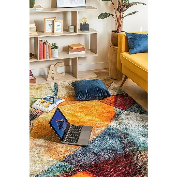 Alfombra de pelo corto Leire - Multicolor, 230 x 160 cm - Alfombra colorida con patrones geométricos, un portátil, almohada y libro. La alfombra domina la habitación y le da un toque moderno.