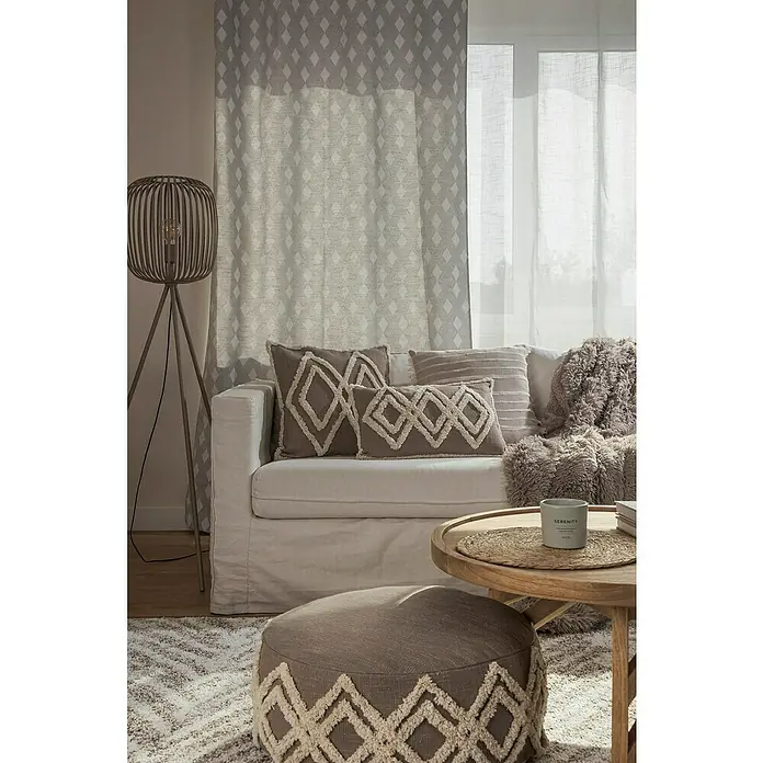 Cortina con ollaos Duko - An x Al: 140 x 260 cm, Perla - Elegante interior de salón con cojines beige, un puf y una alfombra con motivos de rombos para un toque acogedor.