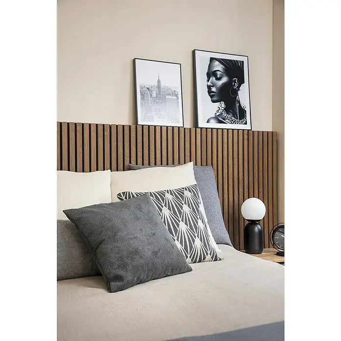 Cojín Pana - 45 x 45 cm, Poliéster, Gris, Cuadrado - Primer plano de una cama con almohadas, un cabecero de madera y dos imágenes enmarcadas arriba, mostrando una decoración de dormitorio acogedora y elegante.