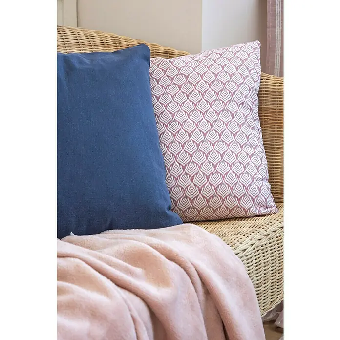 Manta para sofá Chicago - 130 x 150 cm, Poliéster, Rosa - Primer plano de un cojín azul y un cojín rosa con estampado en una silla de ratán, cubierta con una manta rosa.