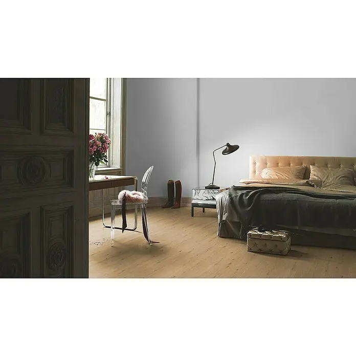 Parador Designbodenmuster Modular ONE Eiche Atmosphere Natur - 200 x 194 x 8 mm, Landhausdiele - Schlafzimmer-Szene mit einem bequemen Bett mit gestepptem Hocker, einem Schreibtisch mit Blumen und einem transparenten Stuhl neben einem Fenster.