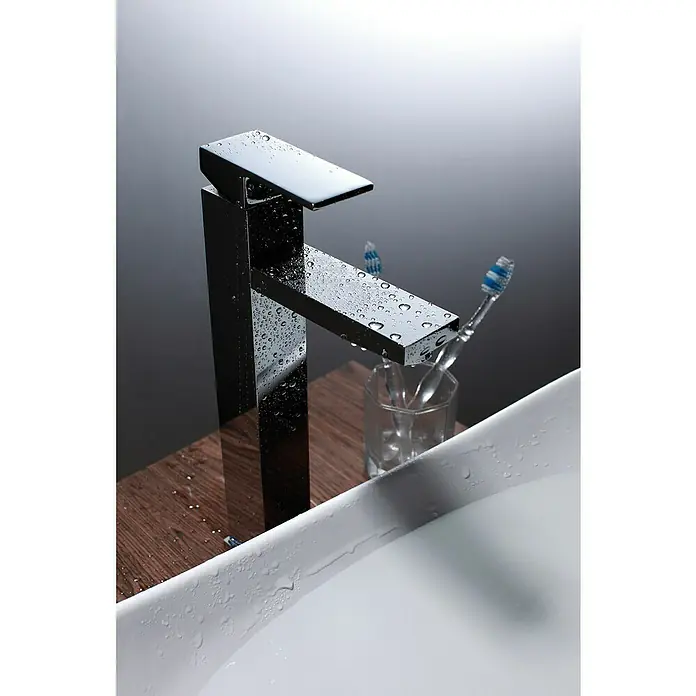 IO Orion Grifo de lavabo - Cromo, Brillante - Grifo de agua moderno y brillante con diseño minimalista, cubierto con gotas de agua, al lado de un vaso de cepillos de dientes en el baño.