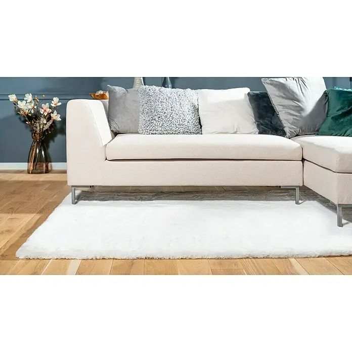 Fellteppich Happy - Elfenbein, 230 x 160 cm, 100 % Polyester (Flor) - Nahaufnahme eines beigen Ecksofas mit silbernen Beinen auf einem weißen Teppich mit verschiedenen Kissen in Grau, Weiß und Grün.