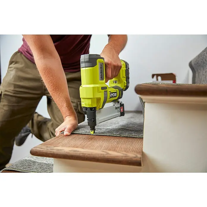 Ryobi ONE+ Akku-Tacker R18GS18-0 - 18 V, Li-Ionen, Ohne Akku - Eine Person befestigt Teppich auf einer Treppe mit einem gelben Ryobi AirStrike Akku-Nagler für präzise Befestigungen.