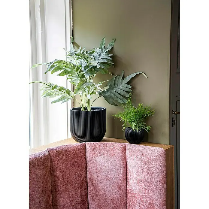 Capi Europe Übertopf rund Nature Groove - Außenmaß (Ø x H): 18 x 15 cm, Schwarz, Polyester - Elegante Kunstpflanzen in schwarzen Pflanzgefäßen, stilvoll auf einem rosa Sofa platziert, bringen einen Hauch von Natur und Design in Ihr Zuhause.
